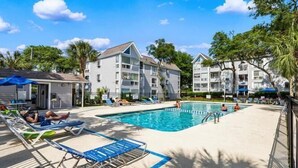 A pool area with lounge chairs, a swimming pool, and multi-story buildings with balconies. - Coastal Getaway Arcadian Dunes #250 -Steps to Sand (Myrtle Beach)