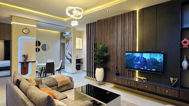 Una sala de estar moderna con un sofá, una mesa de centro, televisión y un área de comedor al fondo.