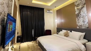 Habitación de hotel moderna con una cama grande, un televisor de pantalla plana, un equipo de aire acondicionado y un plafón.