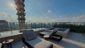Eine Dachterrasse mit Pool, Liegestühlen und einem Hochhaus im Hintergrund.
