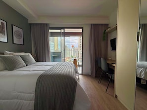 Quarto de hotel com uma cama, uma escrivaninha e vista para a cidade através de uma grande janela.