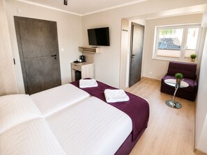 Ein Hotelzimmer mit zwei Betten, einem Fernseher, einem Schreibtisch mit Kaffeemaschine, einem Sessel und einem Fenster mit Blick.