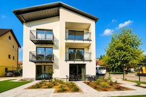 A modern multi-story building with balconies, a patio area with seating, and a well-maintained garden. - Apartment Near the Sea, Breakfast Included (Dziwnów)