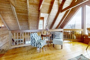 A wooden cabin with a high ceiling, a wooden deck, two patterned chairs, a small table, and a view of the outdoors. - Sweet Scarlet Rose: Hot Tub, View, Pool table (Sevierville)