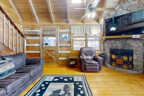 Ein Holzinterieur mit Sofa, Sessel, Kamin und Deckenventilator.