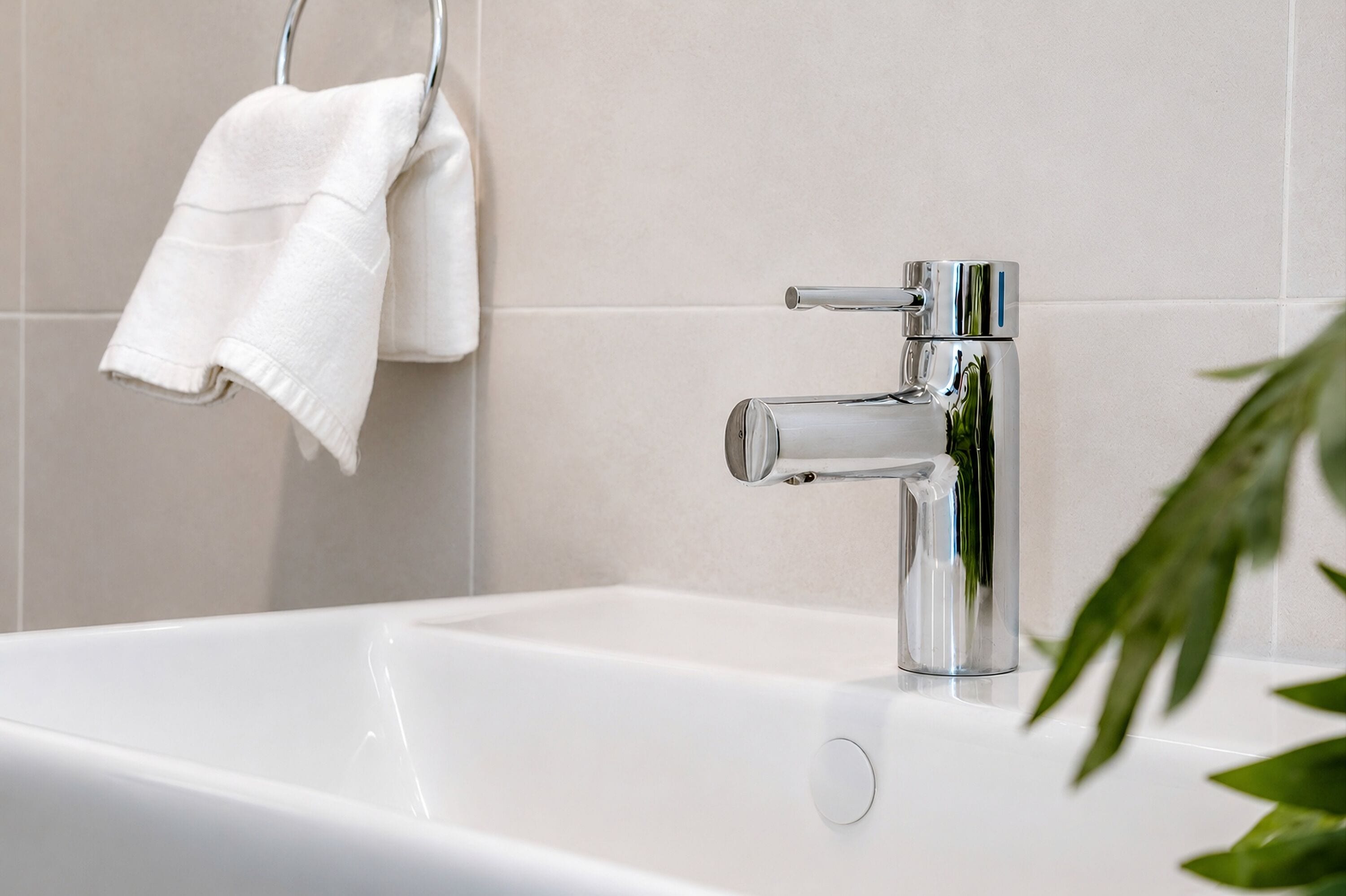 A modern bathroom with a chrome faucet, a white bathtub, and a towel rack with two white towels.
