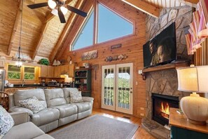 Ein Blockhaus-Interieur mit Kamin, Ledersofa, Küchenbereich und einem großen Fenster.