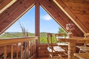Ein Holzinnenraum mit Tisch und Stühlen, ein großes Fenster mit Blick auf Grünflächen und eine weite Landschaft.
