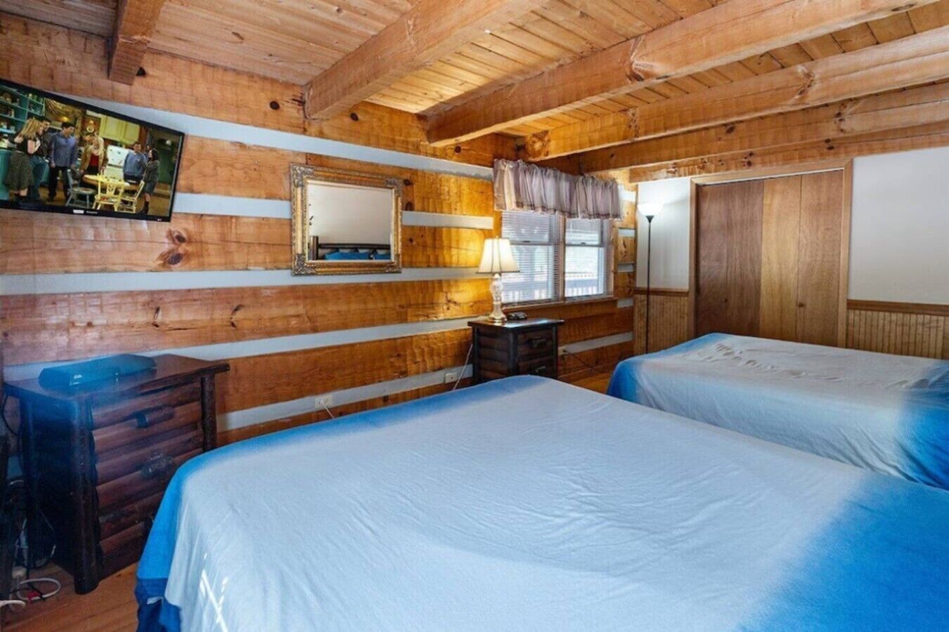 A room with wooden walls, two beds, a dresser, a mirror, and a television.