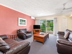 A living room with leather sofas, a coffee table, a TV, and a sliding glass door to a balcony. - Modern Mermaid Beach | Resort Pool & Walk to Beac (Gold Coast)
