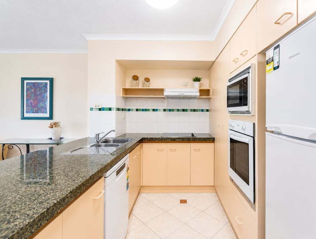 A modern kitchen with a granite countertop, white cabinets, a built-in oven, and a refrigerator.