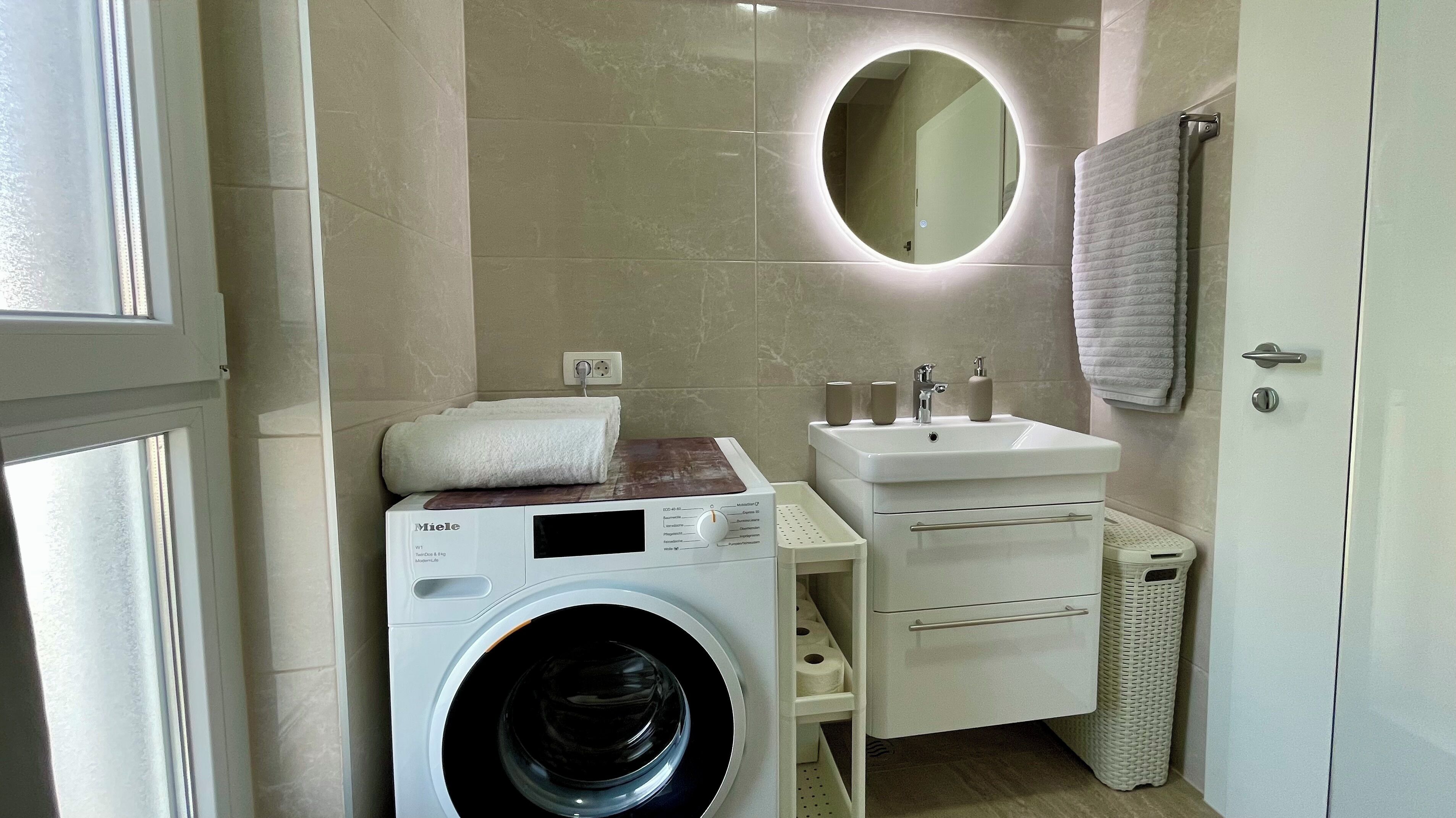 Un baño pequeño con lavadora, lavamanos y espejo.