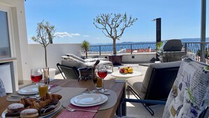 Een dakterras met een ontbijttafel, een barbecue en uitzicht op zee.