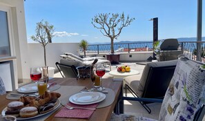 Een dakterras met een ontbijttafel, een barbecue en uitzicht op zee.