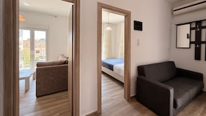 A modern living room with a sofa, a bed, and a dining area visible through a doorway. - Arte Apartments with Parking (Agios Nikolaos)