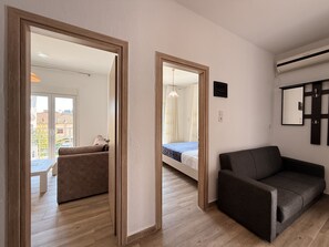 A modern living room with a sofa, a bed, and a dining area visible through a doorway. - Arte Apartments with Parking (Agios Nikolaos)