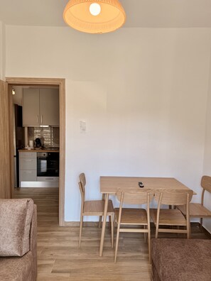 A compact living space with a dining table, two chairs, a sofa, a kitchen area, and a ceiling light fixture. - Arte Apartments with Parking (Agios Nikolaos)
