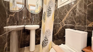 A bathroom with two sinks, a toilet, and a shower curtain with leaf patterns. - Arte Apartments with Parking (Agios Nikolaos)