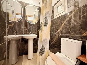 A bathroom with two sinks, a toilet, and a shower curtain with leaf patterns. - Arte Apartments with Parking (Agios Nikolaos)