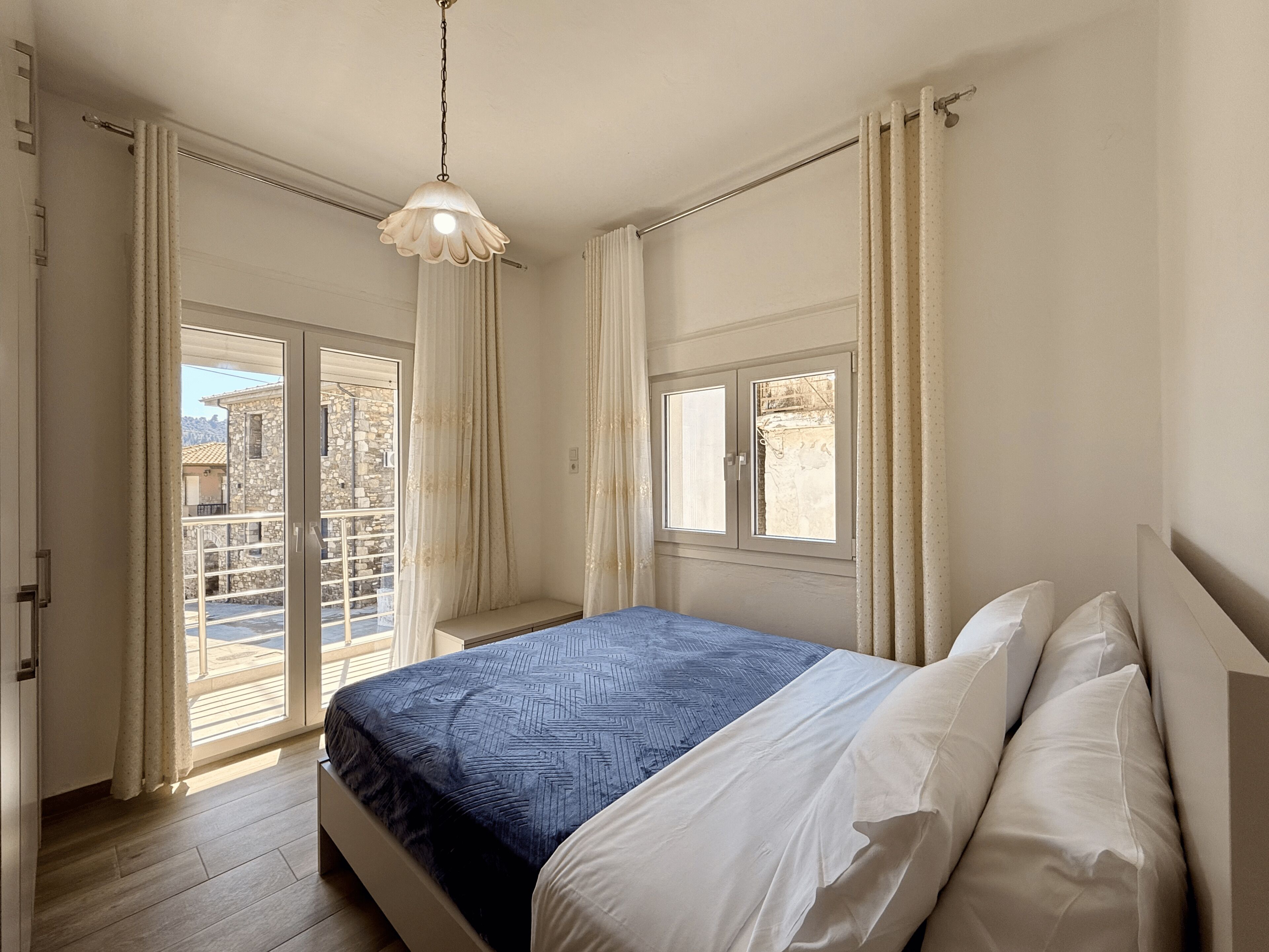 A bedroom with a bed, a hanging light fixture, a window, and a view of the outside.