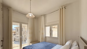 A bedroom with a bed, a hanging light fixture, a window, and a view of the outside. - Arte Apartments with Parking (Agios Nikolaos)