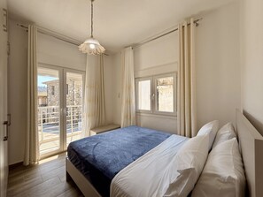 A bedroom with a bed, a hanging light fixture, a window, and a view of the outside. - Arte Apartments with Parking (Agios Nikolaos)