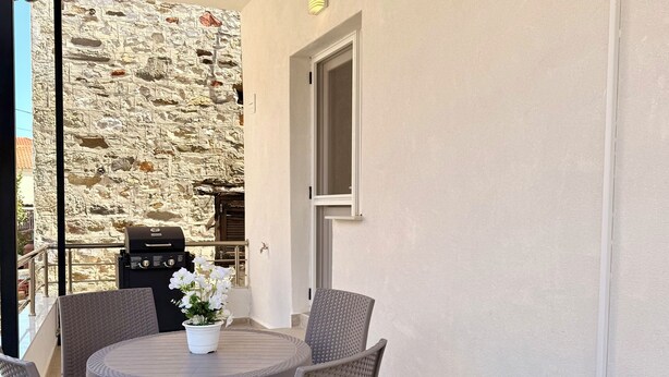 A patio with a round table and four chairs, a stone wall, and a grill. - Arte Apartments with Parking (Agios Nikolaos)