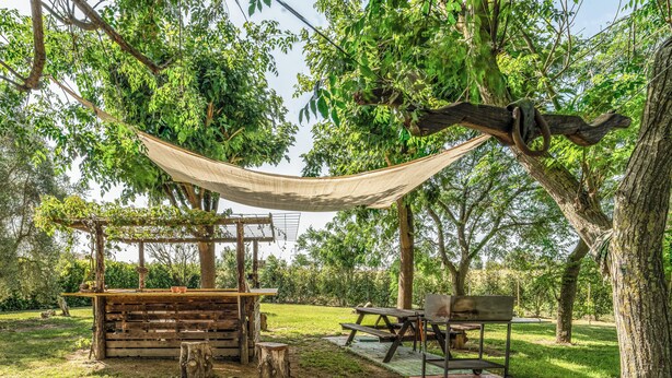A rustic outdoor seating area with a wooden table, benches, and a hammock. - Podere Pala - Pet Friendly (Toscana)
