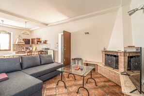 A living room with a sofa, a glass coffee table, a fireplace, and a kitchen in the background. - Podere Pala - Pet Friendly (Toscana)