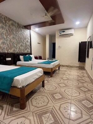 A hotel room with two beds, a ceiling fan, an air conditioning unit, patterned floor tiles, and a wall-mounted TV. - Sree Simran Grand (Hyderabad)