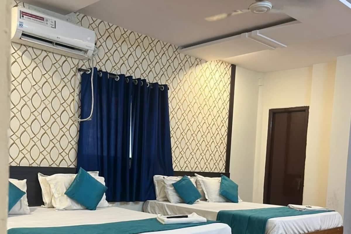 Habitación de hotel con dos camas, aire acondicionado, ventilador de techo y un diseño de pared estampado.