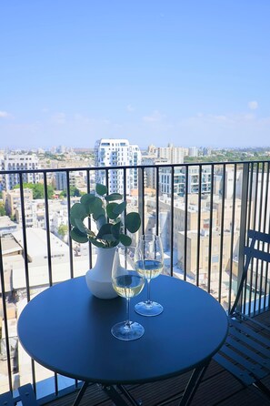 A balcony with a table, two wine glasses, and a potted plant. - High-End 1BR Secure Tower Parking Mamak (Tel Aviv-Yafo)