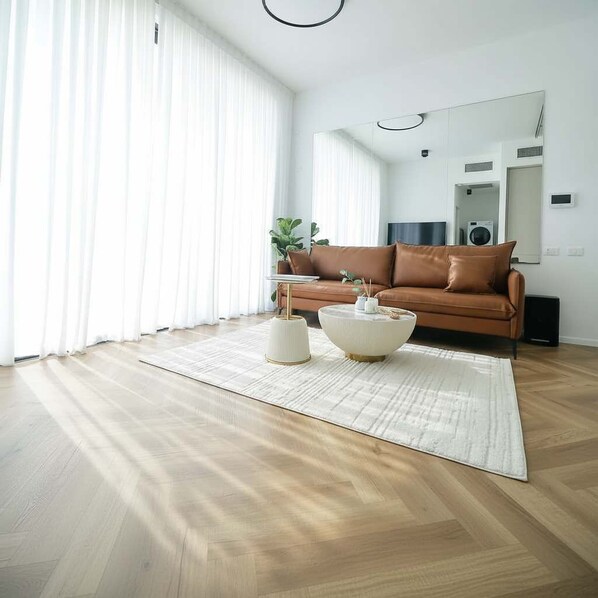 A modern living room with a brown leather sofa, a white rug, and two white side tables. - High-End 1BR Secure Tower Parking Mamak (Tel Aviv-Yafo)