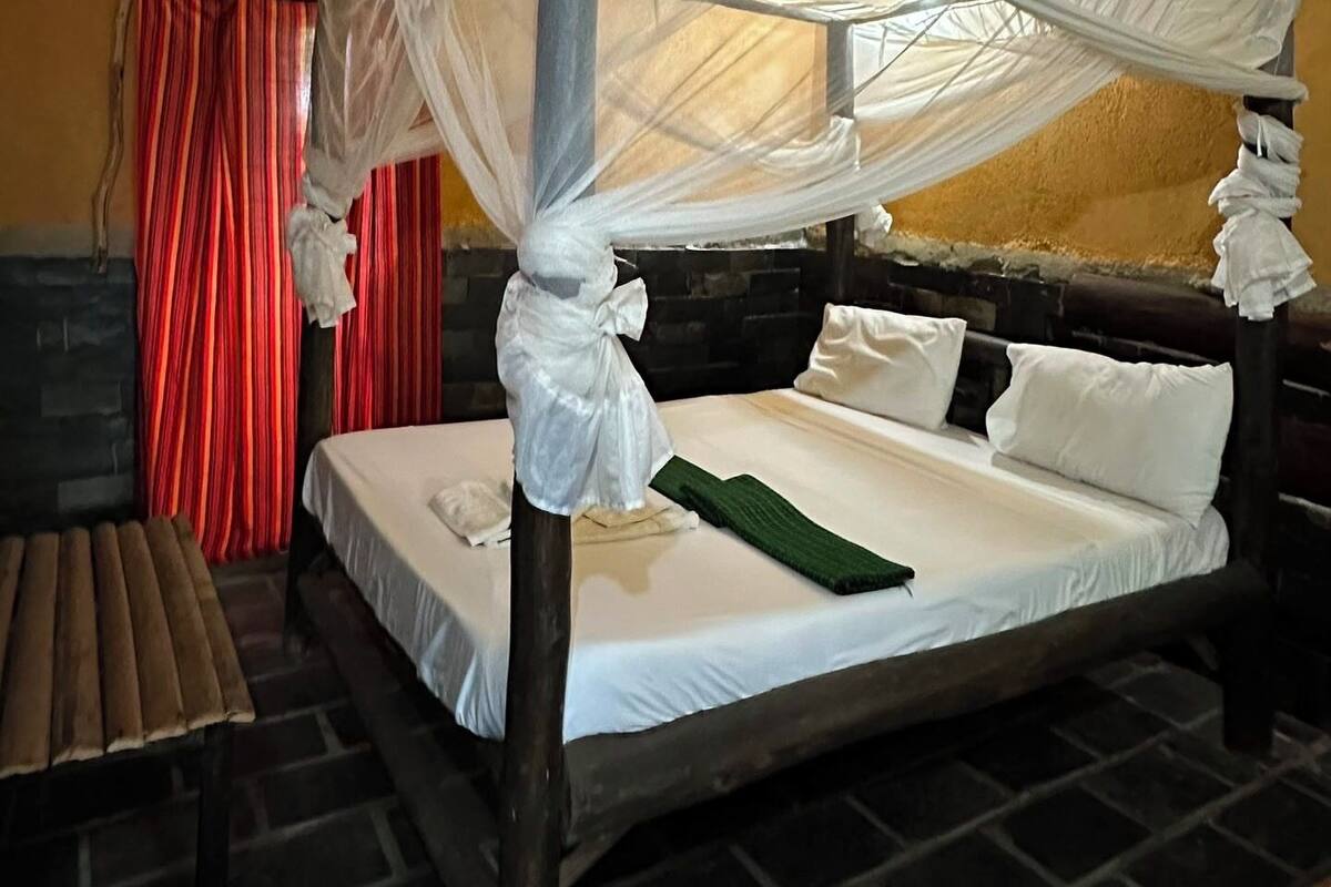 A room with a four-poster bed, a bench, and a small table.