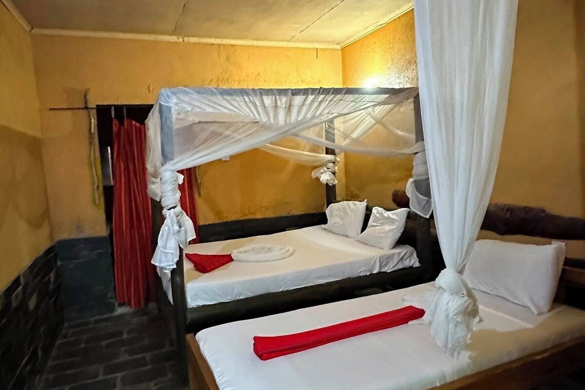 A room with two beds, a stone floor, and a yellow wall.