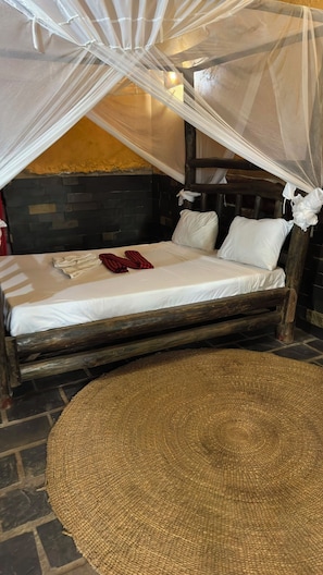A bed with a canopy, a woven rug, and a stone wall.