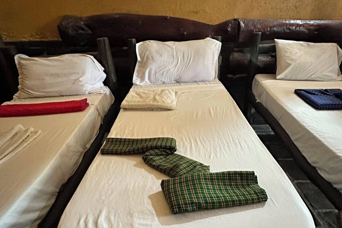 A room with two beds, each with white linens and pillows. There are folded green checkered blankets on one bed.