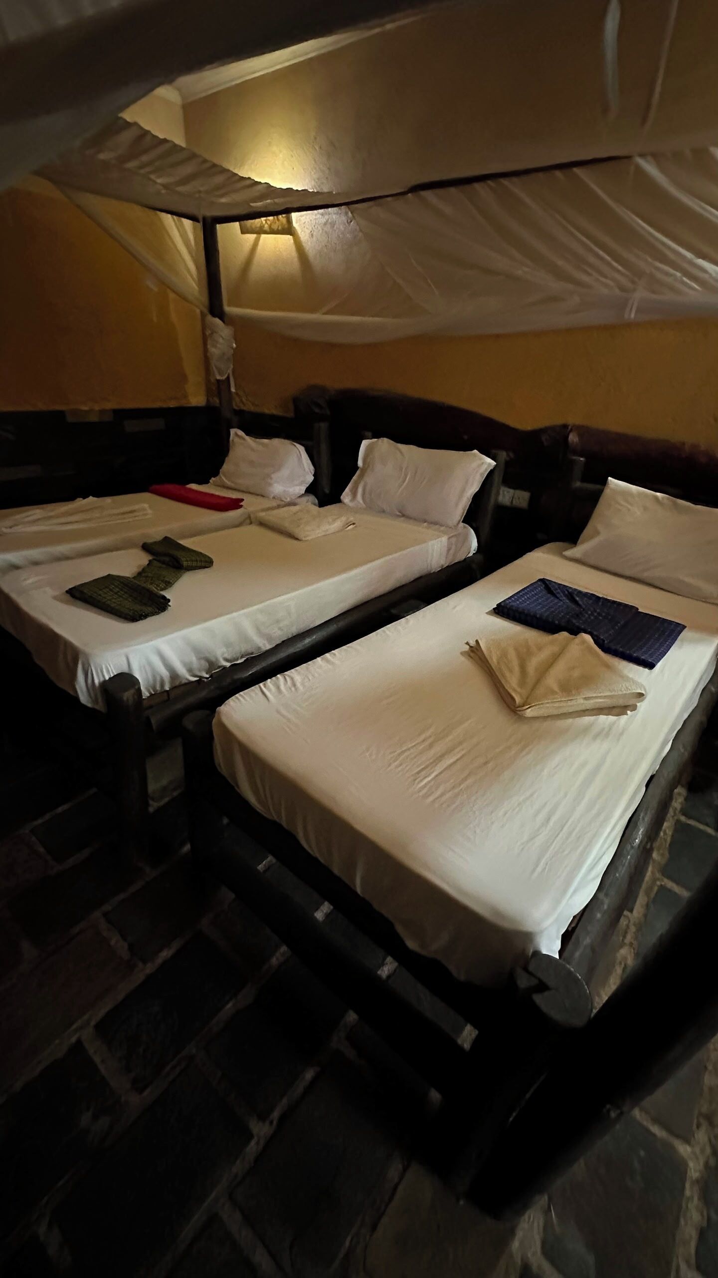 A room with two beds, each with white linens and pillows, a brick floor, and a canopy bed.