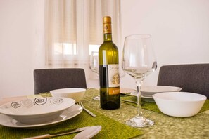 A dining table set with a bottle of wine, glasses, bowls, and cutlery. - Modern apartment with sea view and balcony in Novi Vinodolski (Novi Vinodolski)