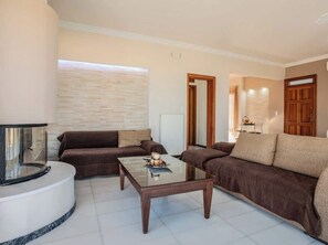 Ein Wohnzimmer mit rundem Couchtisch, zwei Sofas, einem Kamin und einer Tür zu einem weiteren Raum.