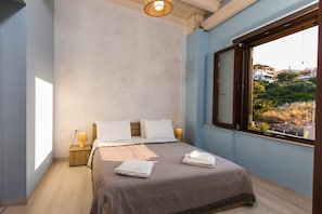 Ein Schlafzimmer mit einem Bett, zwei Kissen, einem Nachttisch mit Lampe und einem Fenster mit Blick.