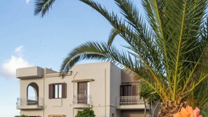 Edifici de dues plantes amb un balcó, un jardí amb una palmera i uns roses.