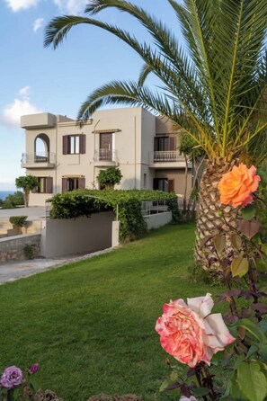 Ein zweistöckiges Gebäude mit einem Balkon, einem Garten mit einer Palme und einem Rosengewächs.