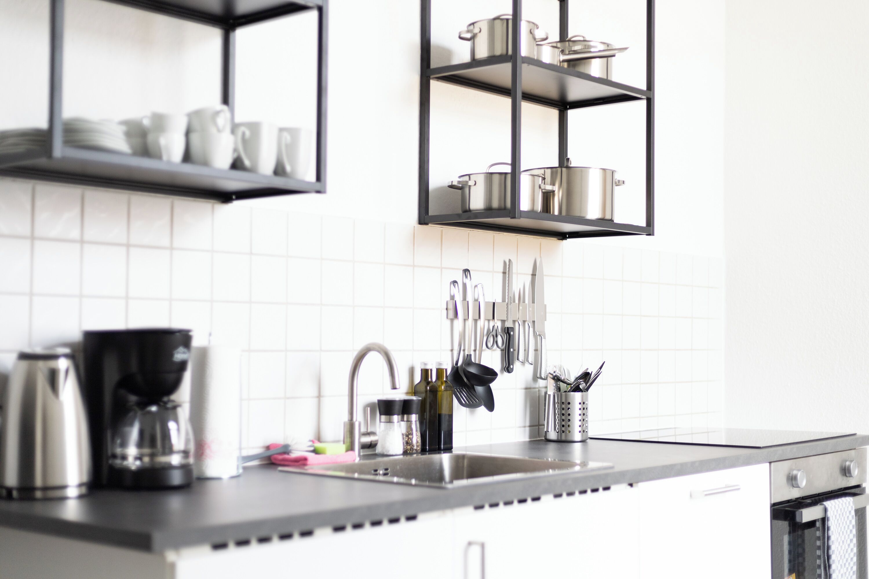 Eine Küche mit Spüle aus Edelstahl, einer Kaffeemaschine und Geschirr, das über der Arbeitsfläche hängt.