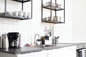 Eine Küche mit Spüle aus Edelstahl, einer Kaffeemaschine und Geschirr, das über der Arbeitsfläche hängt.