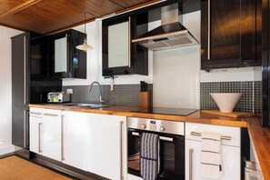 Une cuisine avec des meubles de couleur noire, un plan de travail en bois, une hotte en acier inoxydable et un dosseret carrelé.