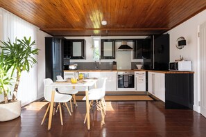A modern kitchen with wooden flooring, a dining table with chairs, a potted plant, and a microwave. - Deck House by the sea (couple or couple + 2 kids) (Emsworth)