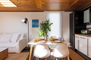A modern kitchen with white cabinets, a dining table with chairs, a plant, and a white sofa in a bright room with wooden ceiling beams. - Deck House by the sea (couple or couple + 2 kids) (Emsworth)