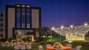 Un espacio para eventos al aire libre con mesas y sillas, un escenario con iluminación y un edificio al fondo.
