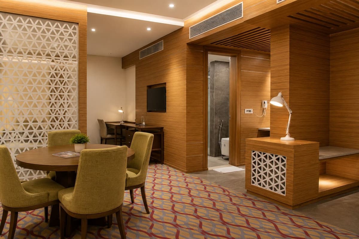 Una habitación de hotel moderna con una pared de acento de madera, un escritorio con lámpara, un pequeño rincón de descanso y una alfombra estampada.